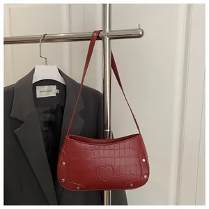 Détail du sac à bandoulière rouge motif crocodile avec patch cœur et rivets argentés