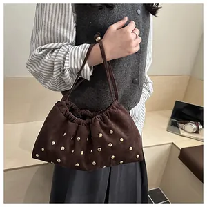 Détail du sac seau en cuir mat marron foncé avec rivets dorés et fermeture à cordon