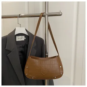 Détail du sac à bandoulière marron motif crocodile avec patch cœur et rivets