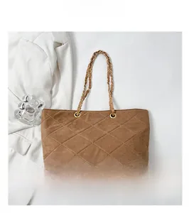 Macro shot of brown suede quilted texture and golden chain strap on shoulder bag