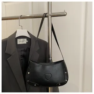 Détail du sac à bandoulière noir motif crocodile avec écusson cœur et rivets argentés
