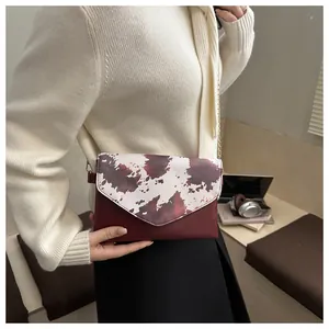 Dettaglio borsa a tracolla bordeaux con patta a stampa mucca e catena dorata elegante