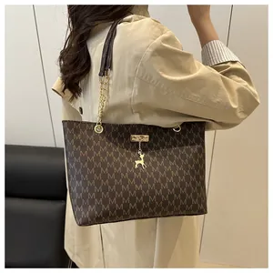 Macro view of brown tote bag showing M-pattern print, gold chain, and deer pendant
