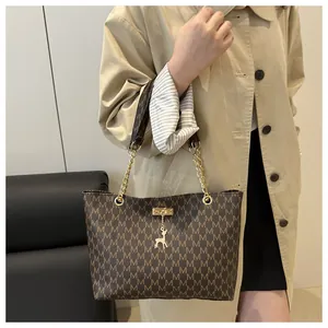 Detail of a large brown tote bag featuring golden chain straps and letter prints