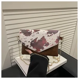 Dettaglio della patta in pelle con stampa mucca e catena dorata sulla borsa