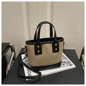 Detail of a beige and black bucket bag with golden rivets and adjustable strap