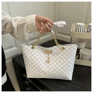 Detail of white tote bag with gray M-letter print and golden deer pendant decoration