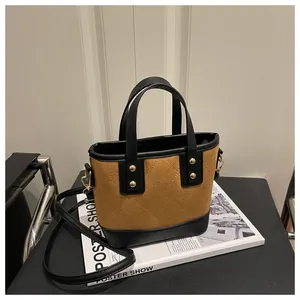 Close-up of brown suede and black leather bucket bag with gold rivets on a magazine