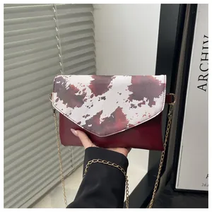 Dettaglio macro della texture in pelle bordeaux e tracolla a catena d'oro di una borsa donna