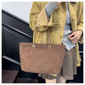 Macro view of dark brown quilted suede shoulder bag with elegant metal chain strap detail
