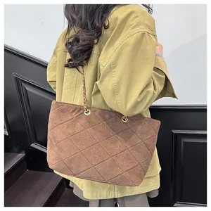 Detail of dark brown quilted suede tote bag with chain strap worn by a model