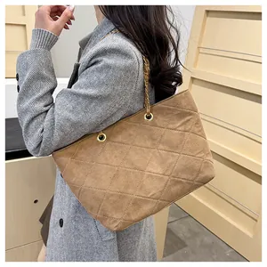 Detail of khaki quilted suede tote bag with woven metal chain strap on grey coat