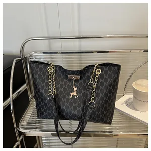 Close-up of black tote bag with white M pattern and elegant gold chain deer charm