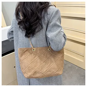 Detailed view of brown suede quilted tote bag with gold chain strap worn by model