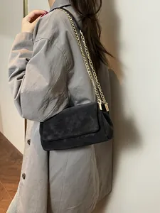 Élégant sac cabas noir en daim avec chaîne dorée porté par un mannequin en décor épuré