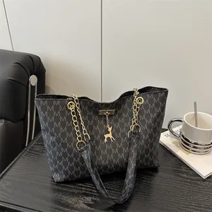 Chic dark grey tote bag with M-print, gold chain straps and a deer charm on a sofa