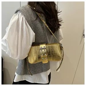 Detail of gold crocodile embossed underarm bag featuring metallic buckle and silver eyelets