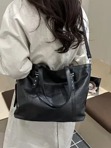 Black leather tote bag with star rivets and fringe zipper worn by a model in a studio