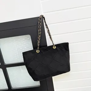Classic black quilted tote bag with golden metal chain strap hanging on a minimal wall