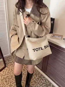 Detailed view of a large beige canvas tote bag with black text on a model shoulder