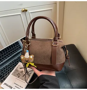 Détail du sac Boston en daim marron avec fermeture éclair dorée et porte-clés ours peluche