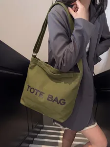 Green canvas tote bag with black print shown worn as a crossbody bag on street