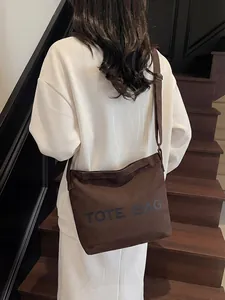 Brown canvas tote bag with adjustable strap shown worn on a model in a casual setting