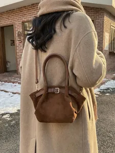 Brown suede bucket bag with pleats and gold buckle shown in an outdoor street setting