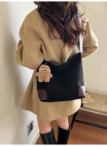 Detail of minimalist black tote bag with brown leather base and plush bear charm