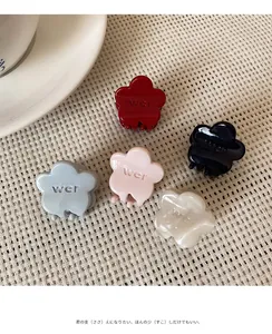 Close-up of five mini floral hair claws in assorted colors on a woven beige background