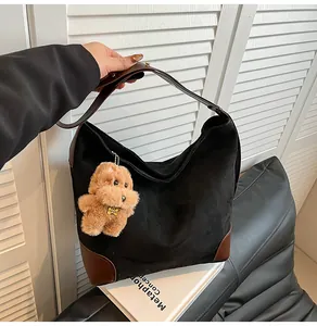 Detail of black suede tote bag with brown leather trim and a cute plush dog pendant