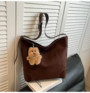 Detail of suede tote bag with brown leather trim and plush teddy bear charm