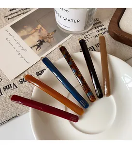 Slim acetate hair clips in six classic colors displayed on a white porcelain dish