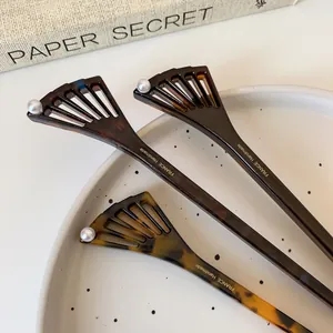 French style tortoise shell acetate hair pin with fan shape and pearl on a white ceramic plate