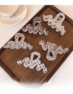 Five assorted wavy claw clips with patterns like cow and leopard print in a wooden tray