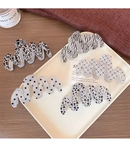 Detail view of five large wave-shaped hair claws with mixed patterns on a white tray
