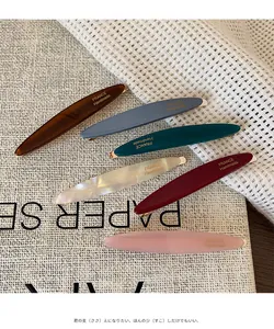 Dettaglio di sei fermagli per capelli in acetato lucido in colori assortiti su lino