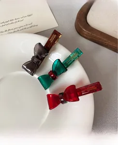 Detail of transparent bow hair clips in grey, green, and red with handmade engraving