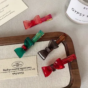 Set of four semi-transparent bow hair clips in red, green, and grey on a wooden tray