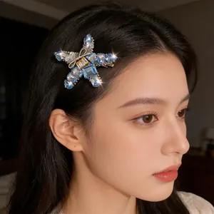 Elegant star-shaped hair clip with blue crystals and gold bow on female model
