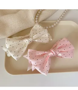 Détail de pinces à cheveux à nœuds en satin à pois beige et rose sur un plateau