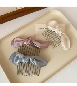 Close-up of three satin bow hair combs in cream, pink, and blue on a beige tray