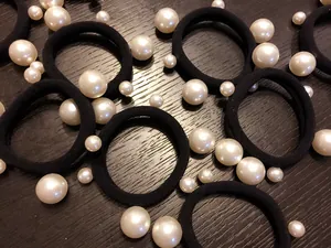 Dettaglio di elastici per capelli neri con perle bianche su fondo in legno