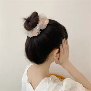 Detailed view of white organza scrunchie with pink floral embroidery on a bun hairstyle