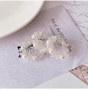Close-up of clear spiral telephone wire hair ties with white pearl decorations on a tray