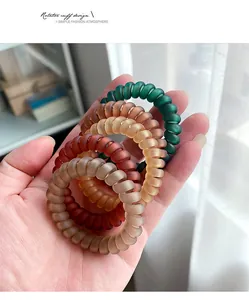 Close-up of matte spiral hair ties in earth tones held in hand for size comparison