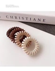 Gros plan de trois élastiques à cheveux spirales tons terre sur un fond minimaliste chic
