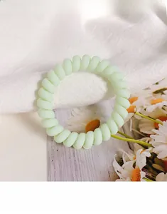 Close-up of light green spiral telephone wire hair tie on a white fabric background