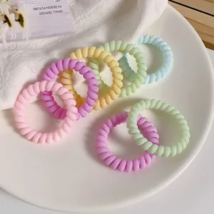 Set of 8 macaron-colored spiral hair ties arranged on a white ceramic plate and fabric
