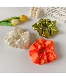 Trois chouchous en satin crème, olive et orange présentés dans un décor style français